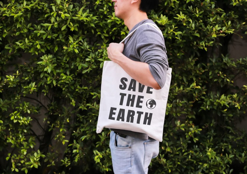 Ein Mitarbeiter trägt eine Stofftasche mit der Aufschrift "Save the Earth" und zeigt damit was Nachhaltigkeit in einem Unternehmen bedeuten kann. 