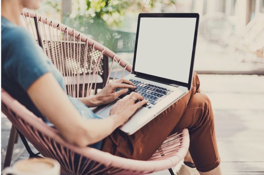 Eine Frau die in Teilzeit arbeitet hat Urlaub und sitz mit ihrem Laptop auf einem Korbstuhl. 